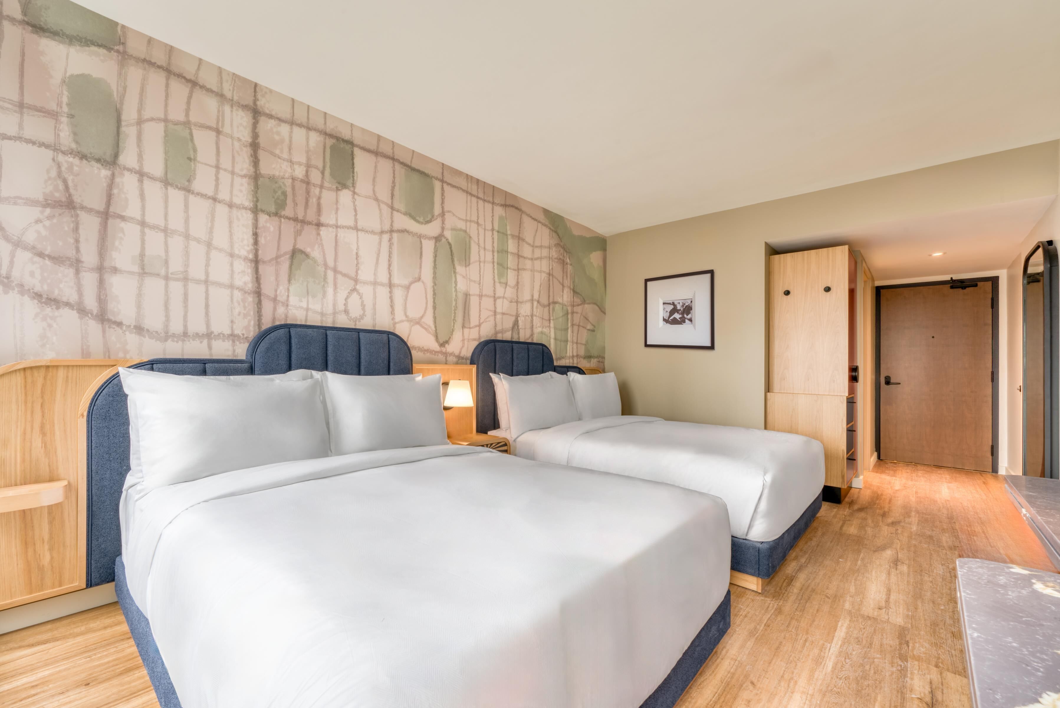 Hotelkamer met twee bedden, een houten hoofdeinde, een muur met een kaartontwerp, een lijst met een afbeelding en een houten deur.