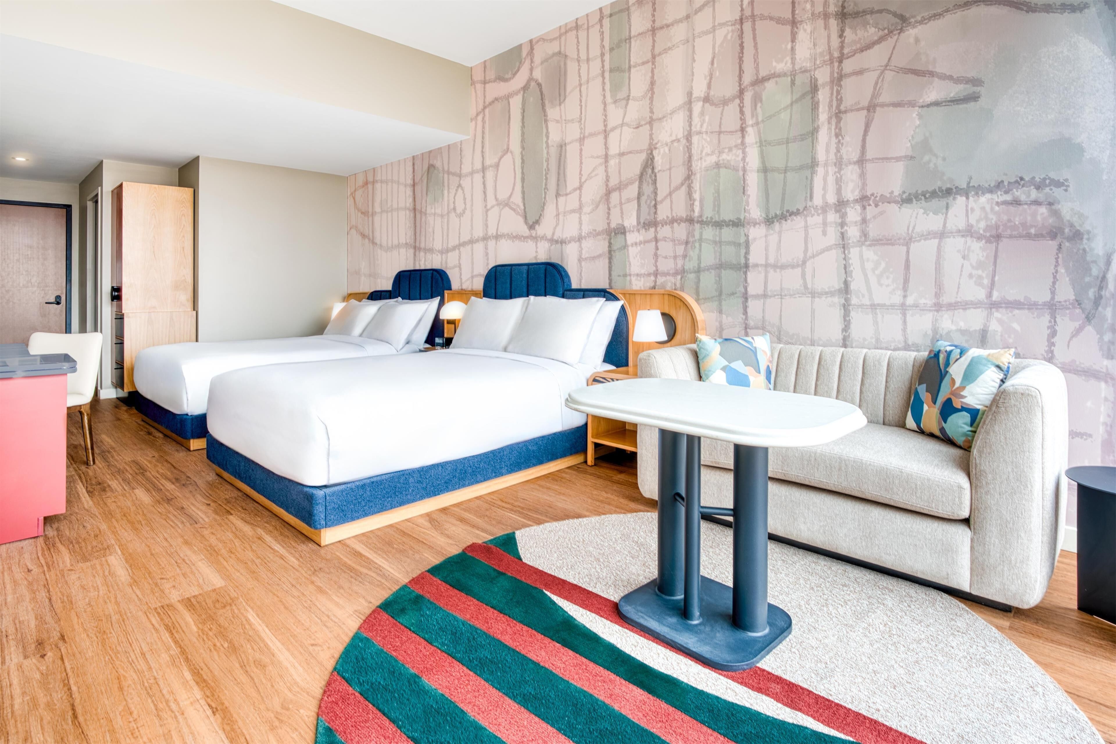 A hotel room with two beds, a sofa, a small table, and a patterned wall.