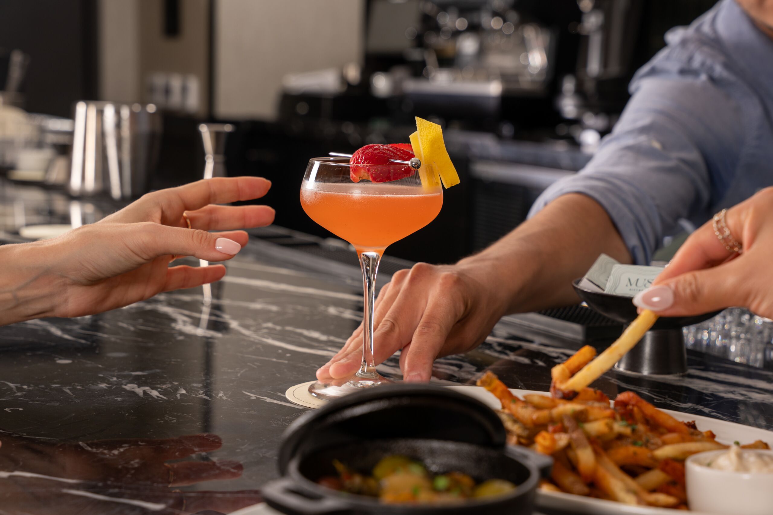 A bar setting with a martini glass, a plate of fries, and a small bowl of sauce.