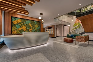 Een receptiezone met een modern design, met een receptiebalie, een zithoek met een bank en voetenbankje, en een trap met een houten leuning.
