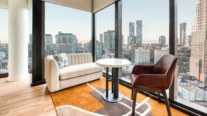 Ein modernes Wohnzimmer mit einer Couch, einem runden Tisch und einem Sessel, mit einem großen Fenster und Blick auf die Stadt.