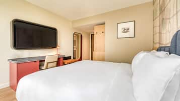 Habitación de hotel con una cama grande, un escritorio con silla, un televisor de pantalla plana, un cuadro en la pared y una puerta de madera.