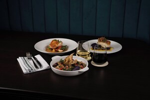 Una mesa de comedor con tres platos de comida, una copa de vino y una servilleta con cubiertos.