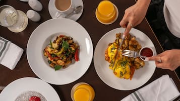 Desayuno con platos de comida, un vaso de zumo de naranja y una taza de café sobre una mesa de madera.