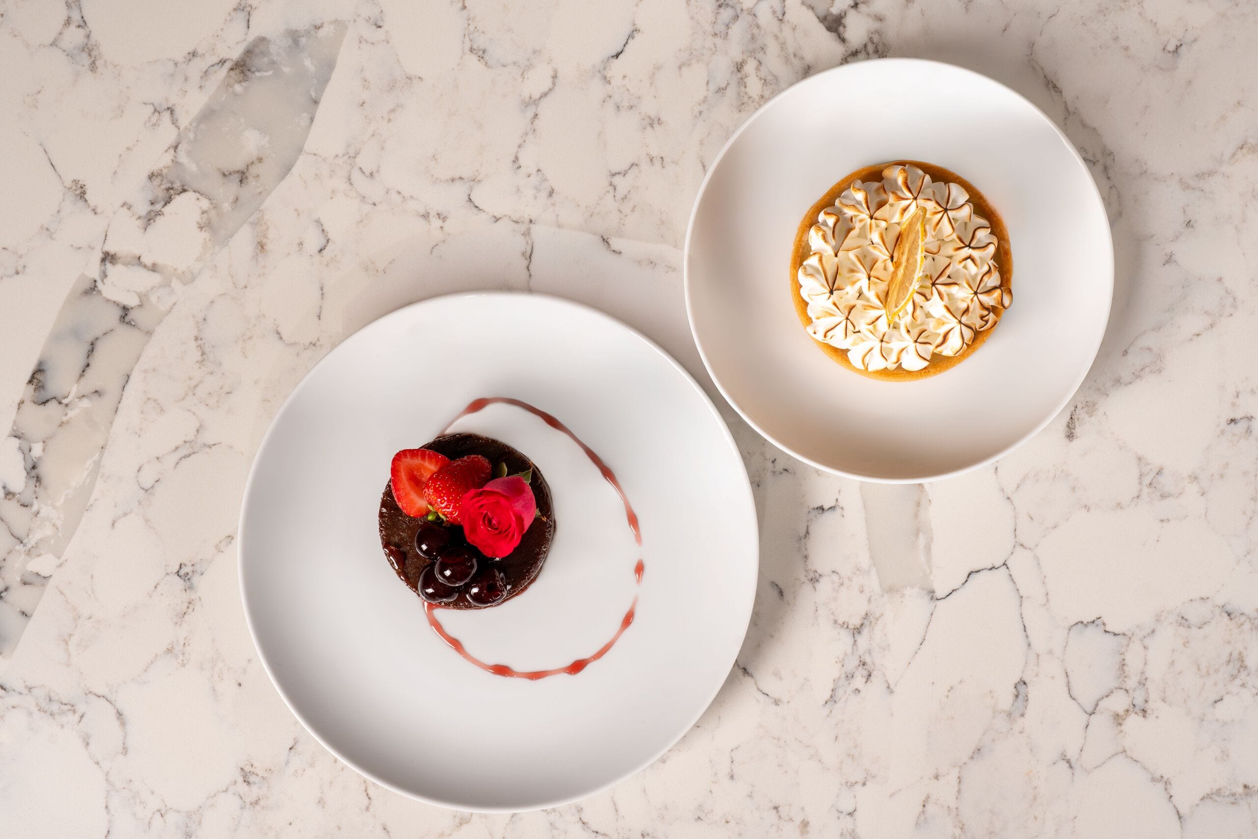 Zwei weiße Teller mit Desserts auf einer Marmorplatte.