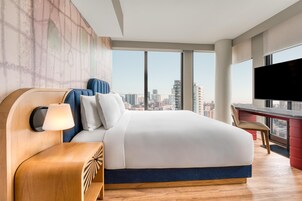 Een moderne hotelkamer met een groot bed, een bureau en uitzicht over de stad.