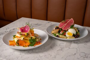 Duas tigelas brancas de salada sobre uma mesa de mármore, com um sofá de couro marrom ao fundo.