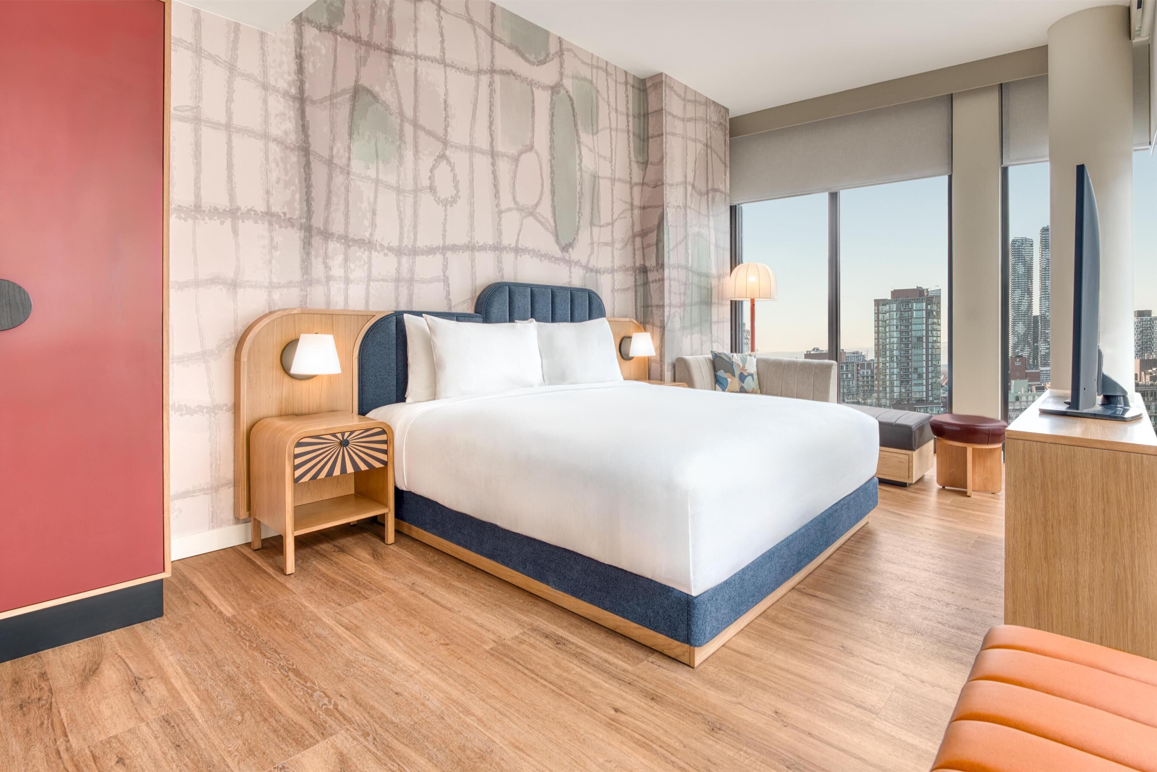 Een moderne hotelkamer met een groot bed, houten nachtkastjes, een bureau en uitzicht op de stad.