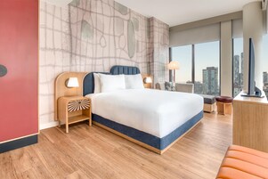 Een moderne hotelkamer met een groot bed, houten nachtkastjes, een bureau en uitzicht op de stad.