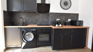 A compact kitchen with a dishwasher, washing machine, oven, microwave, and a coffee maker. - Arum Suite with terrace (Roanne)