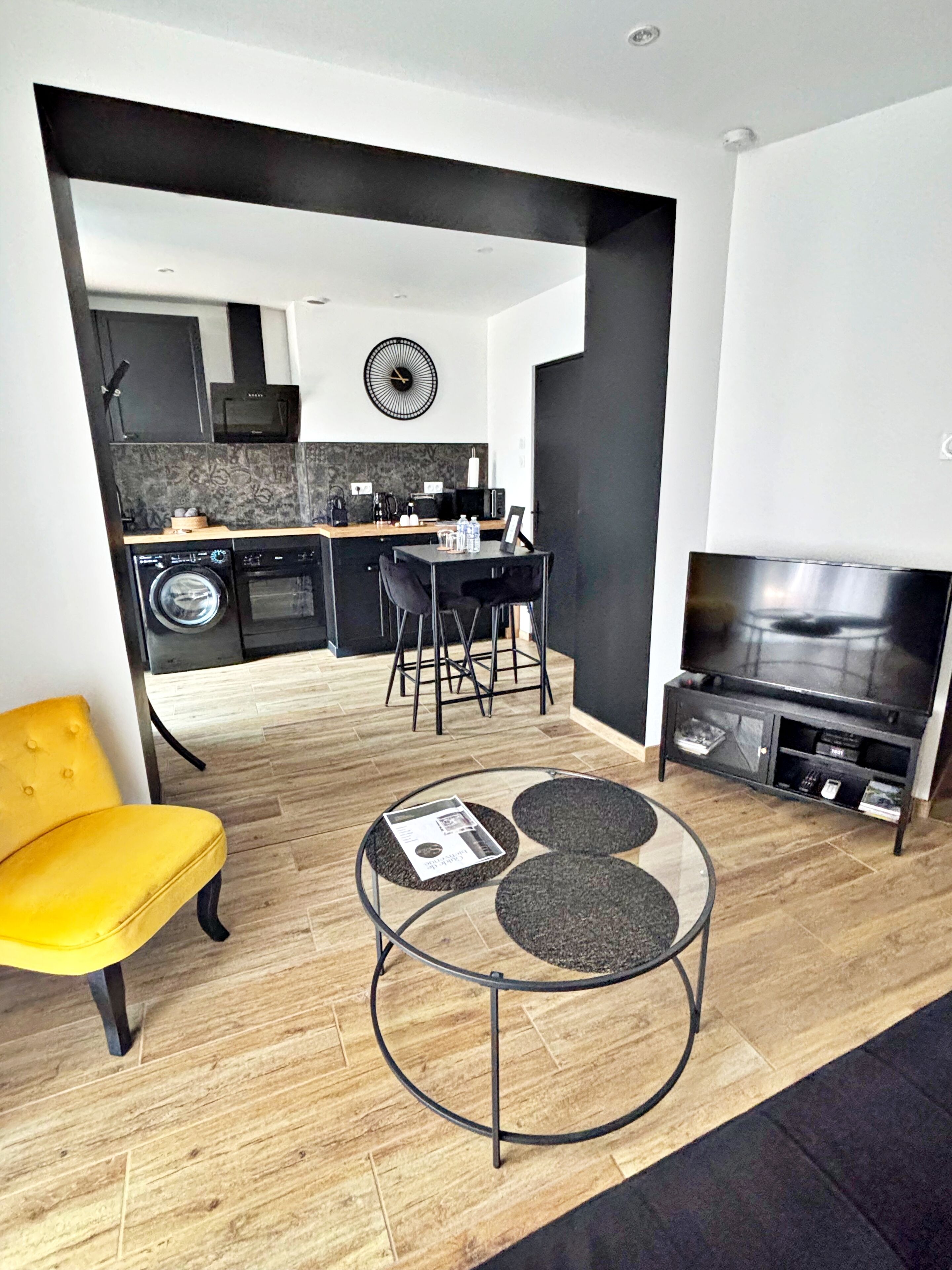 Un salon moderne avec un fauteuil jaune, une table basse en verre et un meuble TV sur lequel est posé un téléviseur à écran plat.