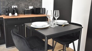 A modern kitchen with dark cabinetry, a wooden countertop, and a dining area with a black table and chairs. - Arum Suite with terrace (Roanne)