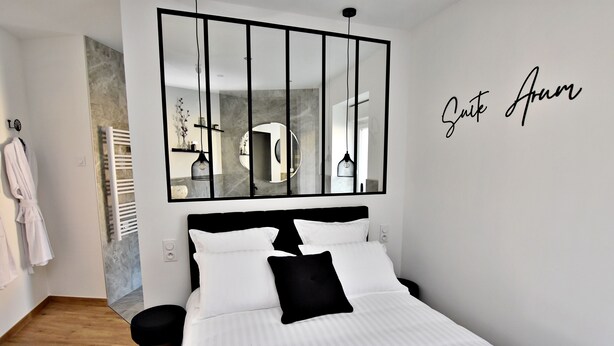 A modern bedroom with a large bed, a black and white color scheme, a mirror with a black frame, and a wall-mounted sign that reads "Suite Arm." - Arum Suite with terrace (Roanne)