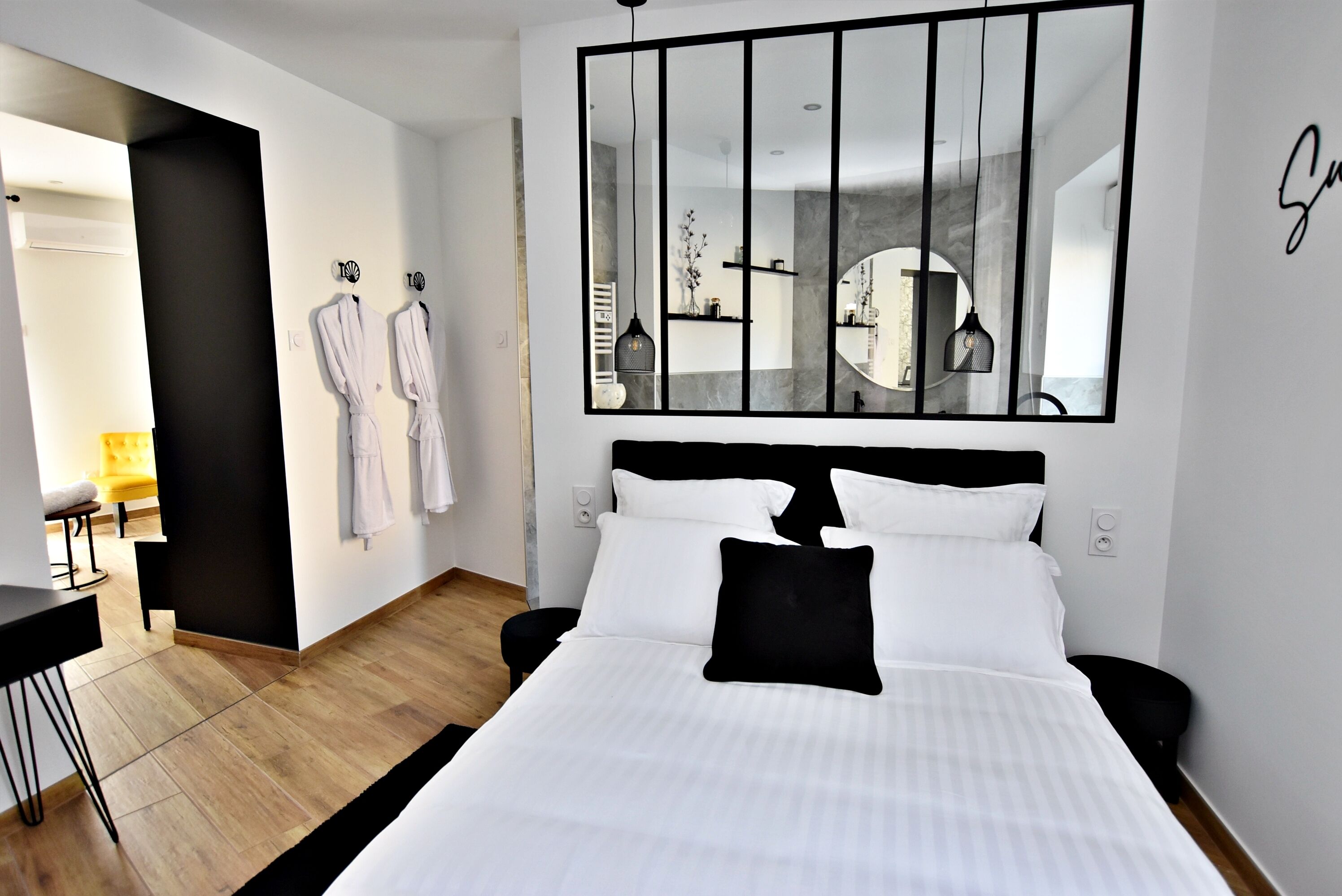 Ein modernes Hotelzimmer mit einem großen Bett, einer schwarz-weißen Farbgestaltung, einem großen Spiegel und Blick ins Badezimmer.