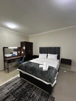 Una habitación de hotel moderna con una cama grande, un escritorio, una silla, un armario y un espejo.