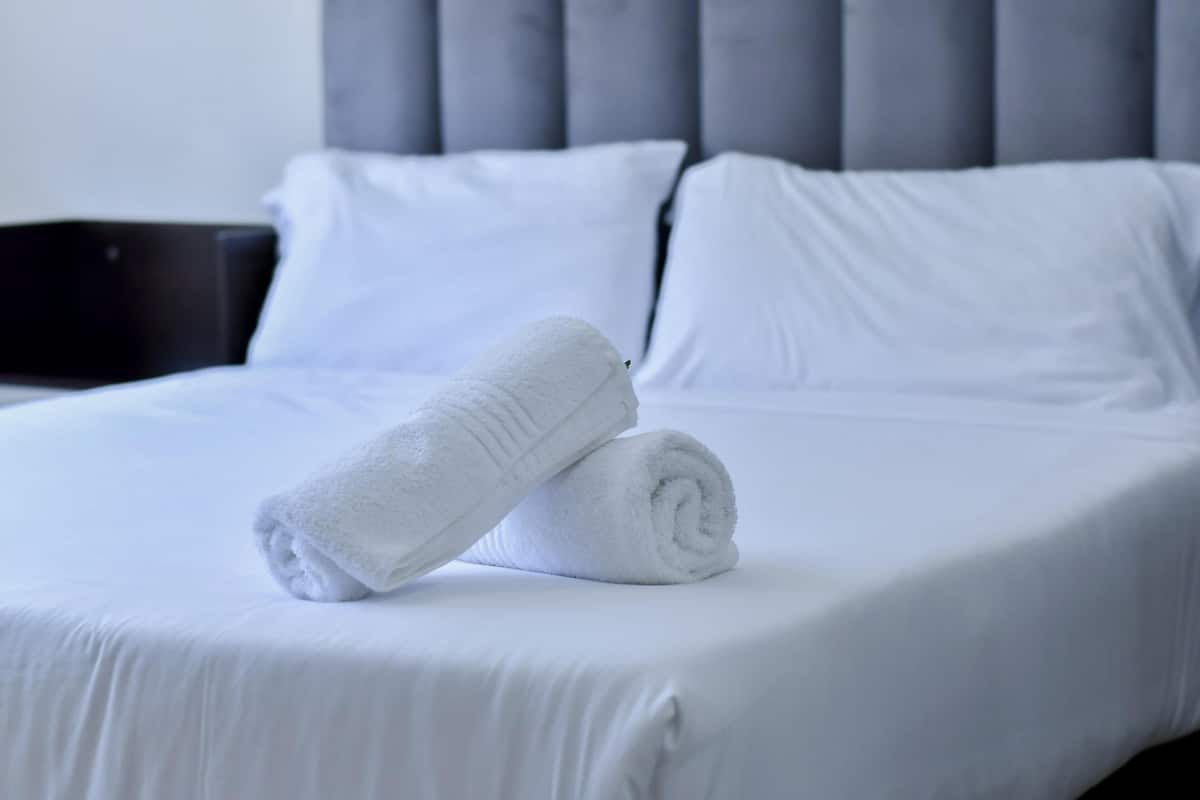 A neatly made bed with white linens and pillows, a grey upholstered headboard, and a black nightstand.