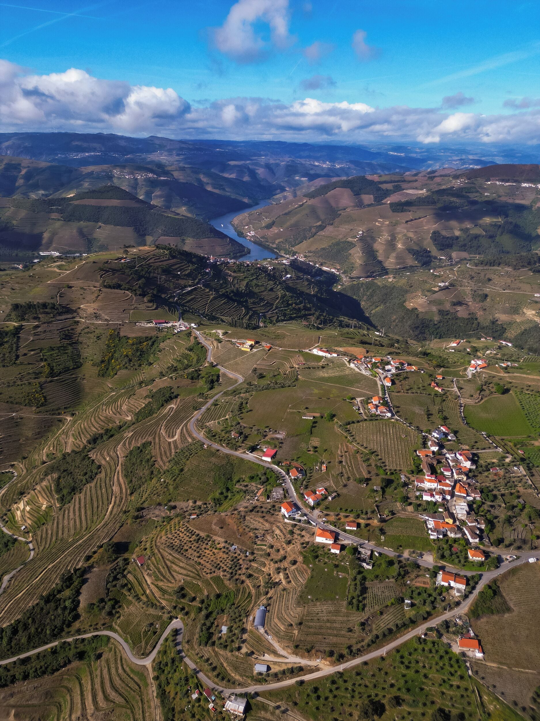 An aerial view of a rural landscape with terraced fields, a river, and a small village with red-roofed buildings.