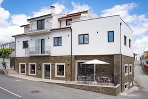Un bâtiment à deux étages doté d’un balcon, d’une terrasse avec des sièges extérieurs et d’une façade en pierre.