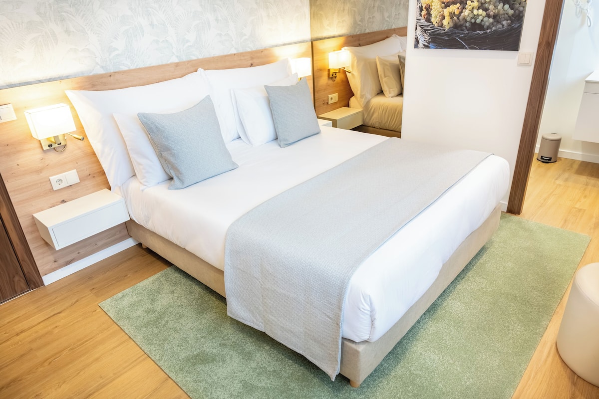 Una cama bien hecha con alfombra verde, cabecera de madera y lámparas de noche.