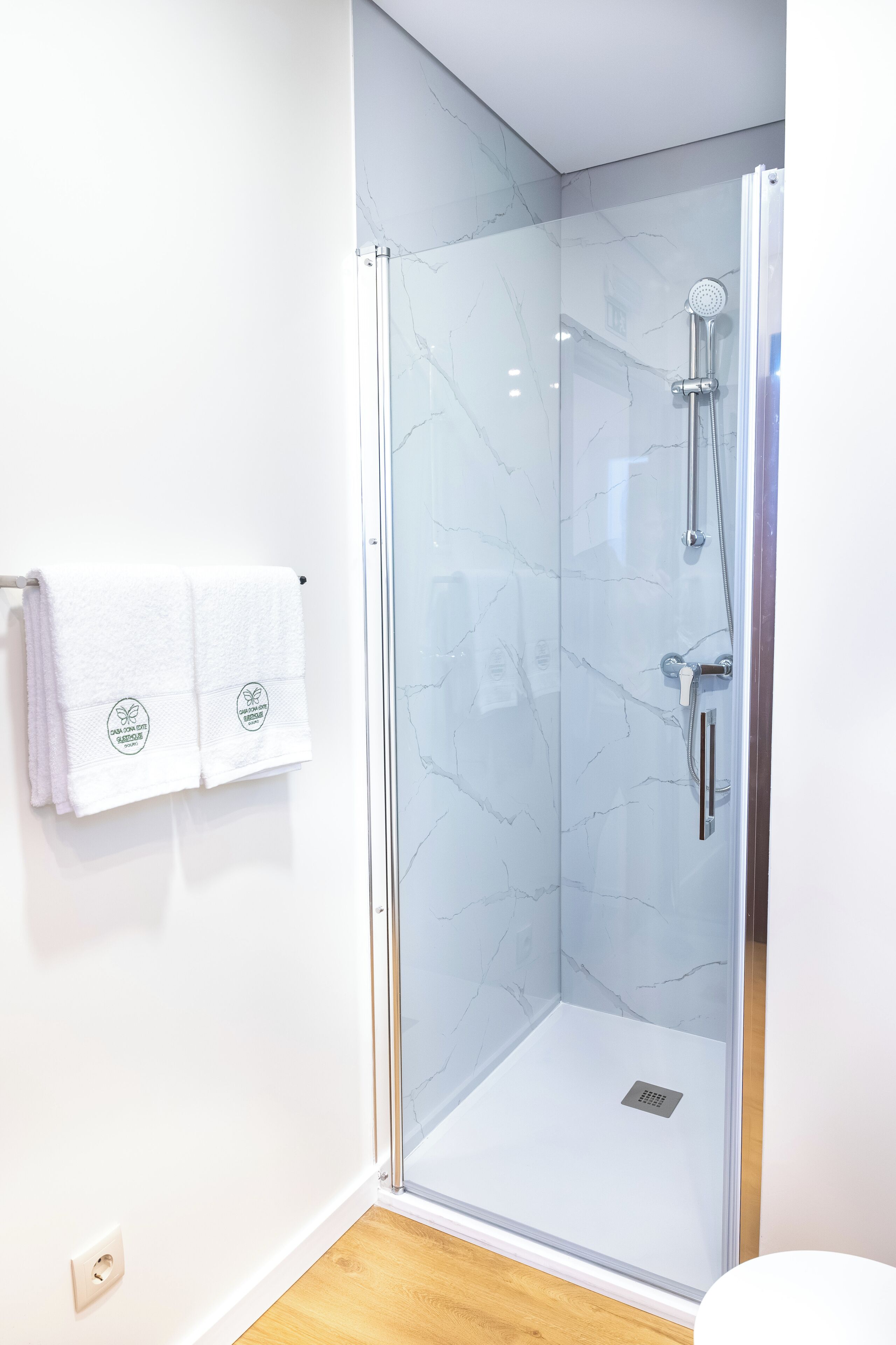 Ein modernes Badezimmer mit einer Glaskabine zur Dusche, weißen Marmorwänden und einem Holzboden.