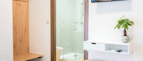 A modern bathroom with a shower, a toilet, and a sink. There is a wooden cabinet and a television mounted on the wall.