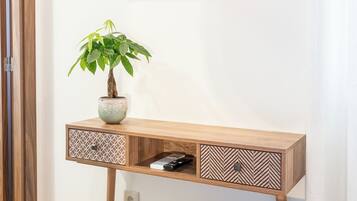 Quarto moderno com escrivaninha de madeira, televisão na parede, planta em vaso e lixeira.