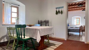 Un coin repas avec une table dressée pour deux personnes, une fenêtre avec des rideaux et une vue sur une autre pièce.