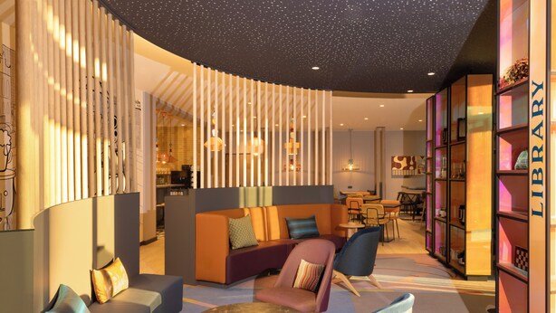 Un espace de détente moderne comprenant des sièges, une table ronde et une bibliothèque portant l’inscription « BIBLIOTHÈQUE ».