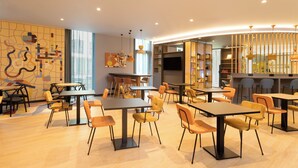 Un restaurant moderne doté de nombreuses tables et chaises, d’une grande fenêtre et d’un mur orné d’œuvres d’art abstrait.