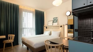 Une chambre d’hôtel comprenant un lit, un bureau, une chaise, une fenêtre avec des rideaux et une kitchenette.