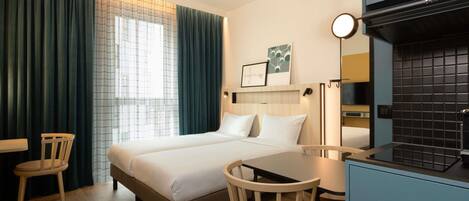 Una habitación de hotel con cama, escritorio, silla, ventana con cortinas y kitchenette.
