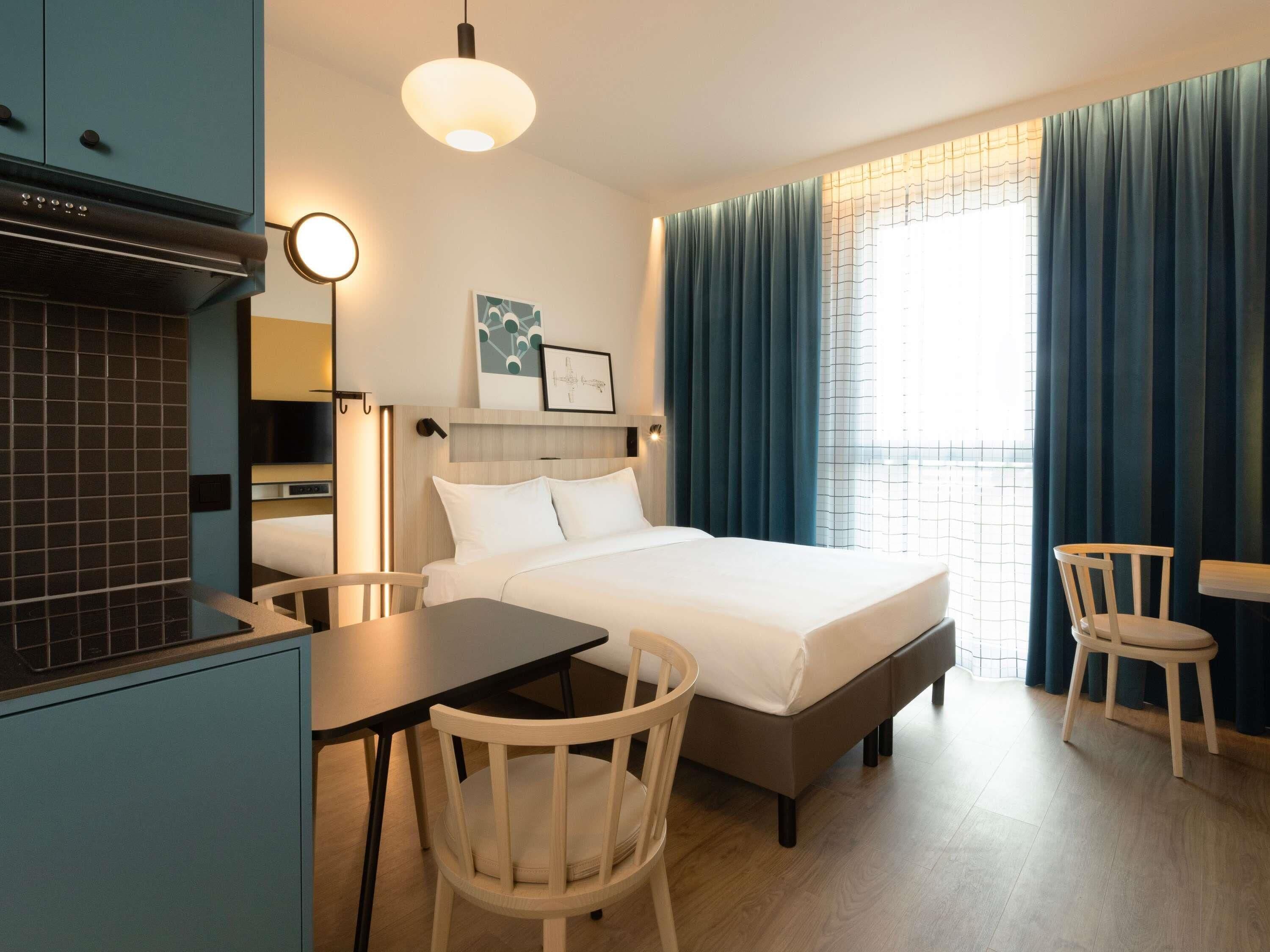 Ein Hotelzimmer mit Bett, Schreibtisch, Stuhl, Fernseher und einem Fenster mit Vorhängen.