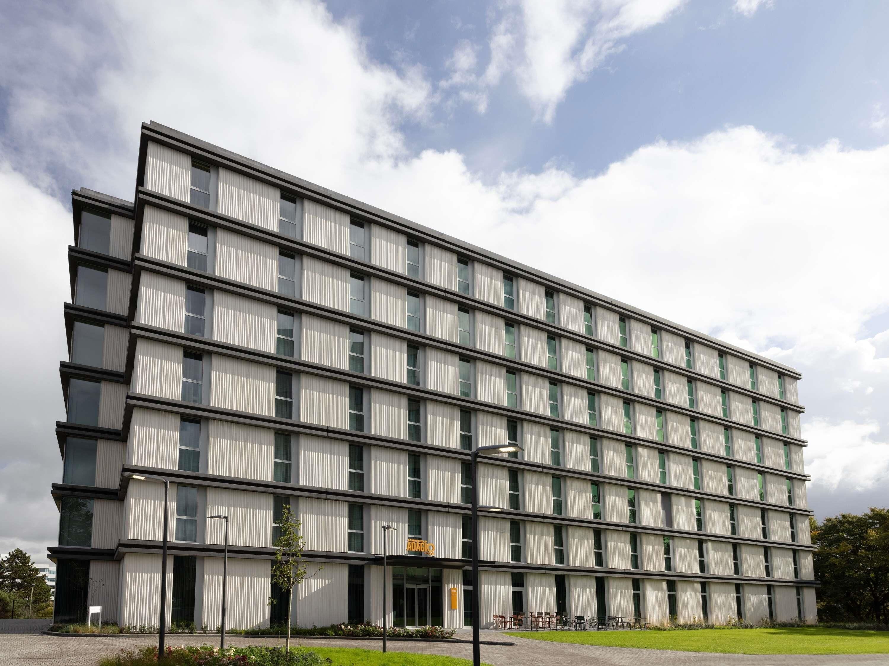 A modern multi-story building with a flat facade, large windows, and a covered entrance area with seating.