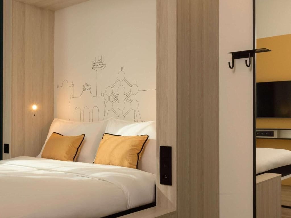 Una habitación de hotel moderna con una cama grande, un televisor de pared y un mural con un paisaje urbano.