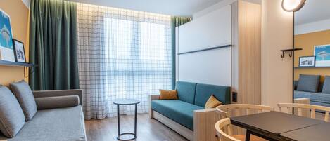 Een moderne woonkamer met een bank, een kleine ronde tafel en een eettafel met stoelen.