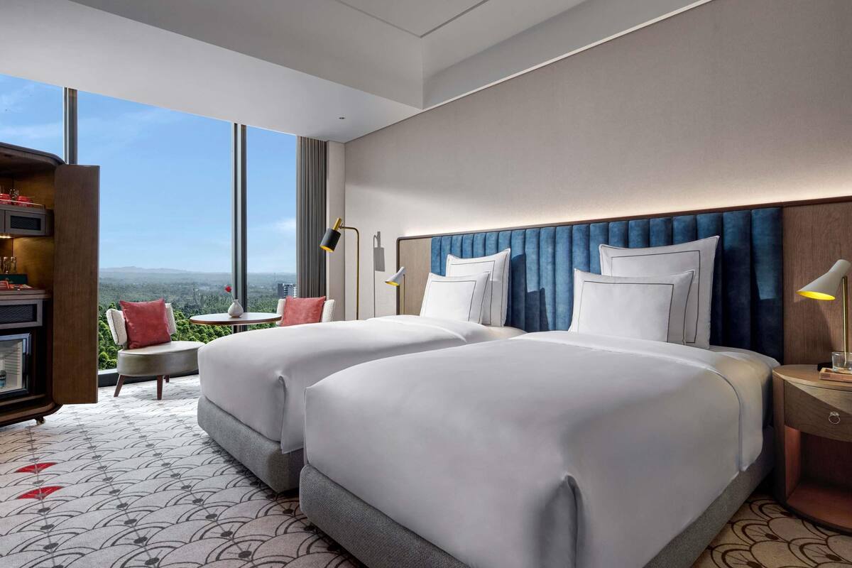 Une chambre d’hôtel avec deux lits, un bureau et une vue sur la ville.