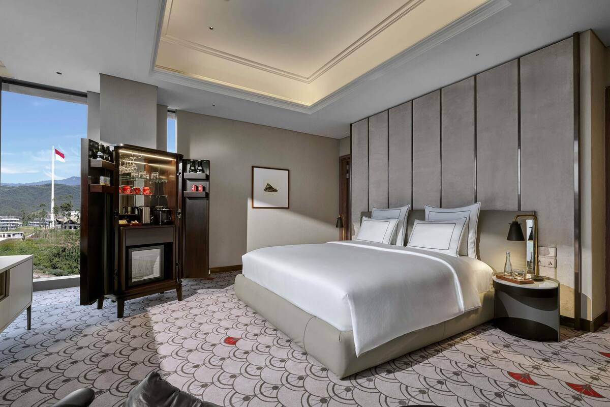 Une chambre d’hôtel moderne dotée d’un grand lit, d’un minibar, d’un bureau et offrant une vue sur la ville.