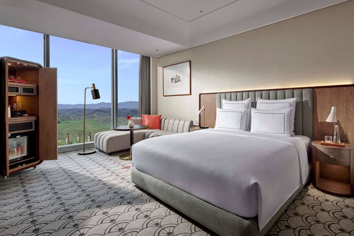 Une chambre d’hôtel moderne dotée d’un grand lit, d’un coin salon, d’un minibar et offrant une vue sur les montagnes.