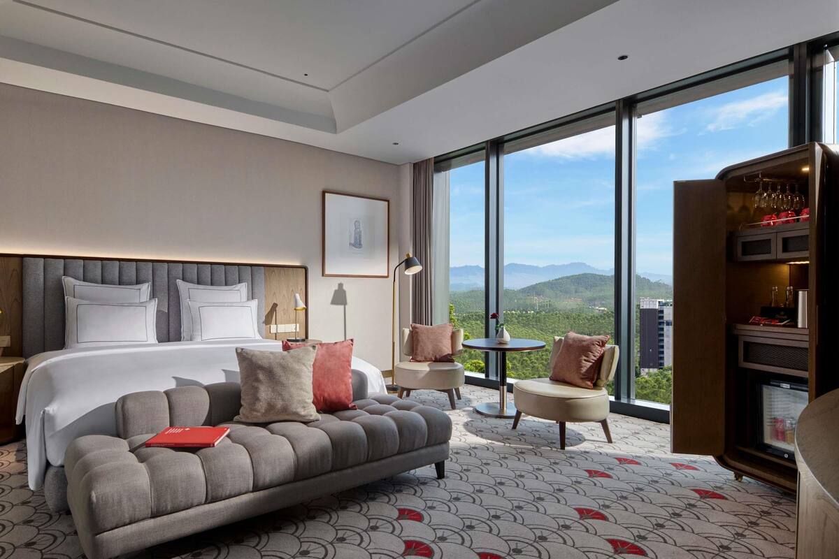 Une chambre d’hôtel avec un grand lit, un canapé, une petite table et un mini-bar. La chambre dispose de grandes fenêtres offrant une vue sur les montagnes.