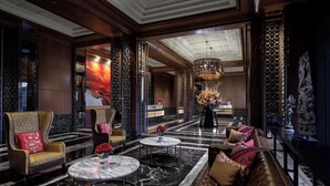 Un hall d’entrée luxueux avec un sol en marbre, un espace de détente central comprenant un canapé et des fauteuils, un comptoir de réception et un lustre décoratif.