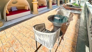 An outdoor seating area with cushioned benches and a glass table, surrounded by a red canopy and stone flooring. - Espana Condo Resort Pattaya Office (Pattaya)