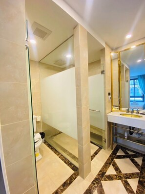 A modern bathroom with a glass shower enclosure, a white sink with a gold frame, and a patterned floor. - Espana Condo Resort Pattaya Office (Pattaya)