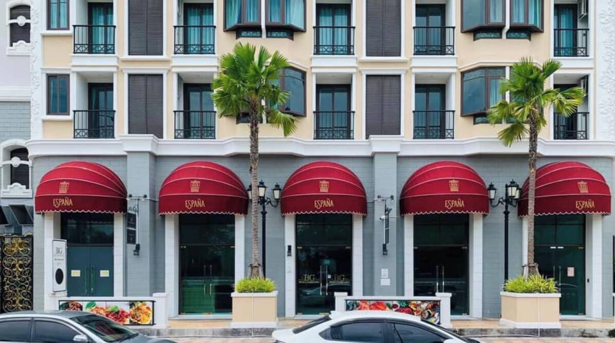 A hotel facade with multiple red awnings labeled "ESPAÑA" and a row of palm trees.