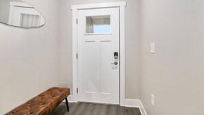 Un couloir avec une porte blanche, un banc et un miroir fixé au mur.