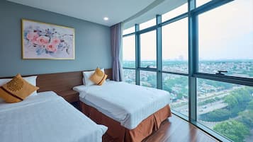Hotellihuone, jossa on kaksi sänkyä, suuri ikkuna, josta on näkymä kaupunkiin, ja seinällä oleva kukka-aiheinen taulu.