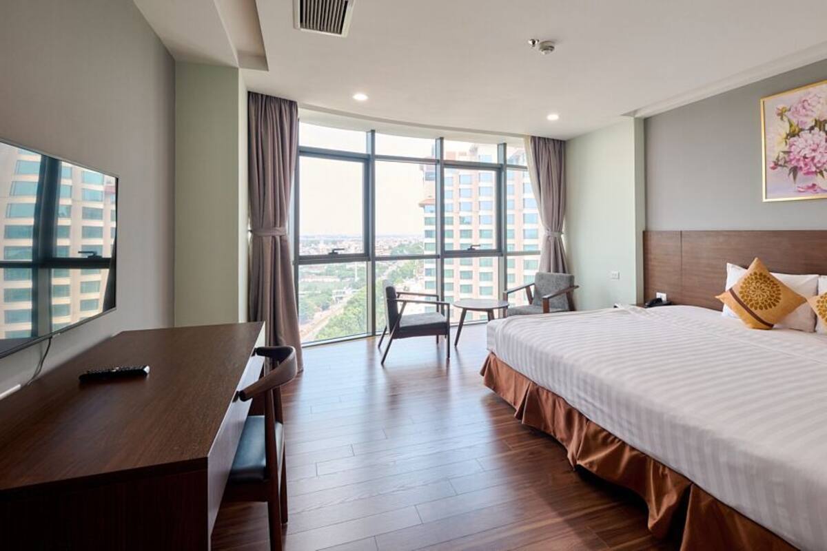 A hotel room with a large bed, a desk, a chair, and a TV.