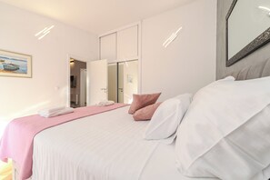 A hotel room with a bed, a pink blanket, a white pillow, and a painting on the wall. - Apartments Grbic (Privlaka)