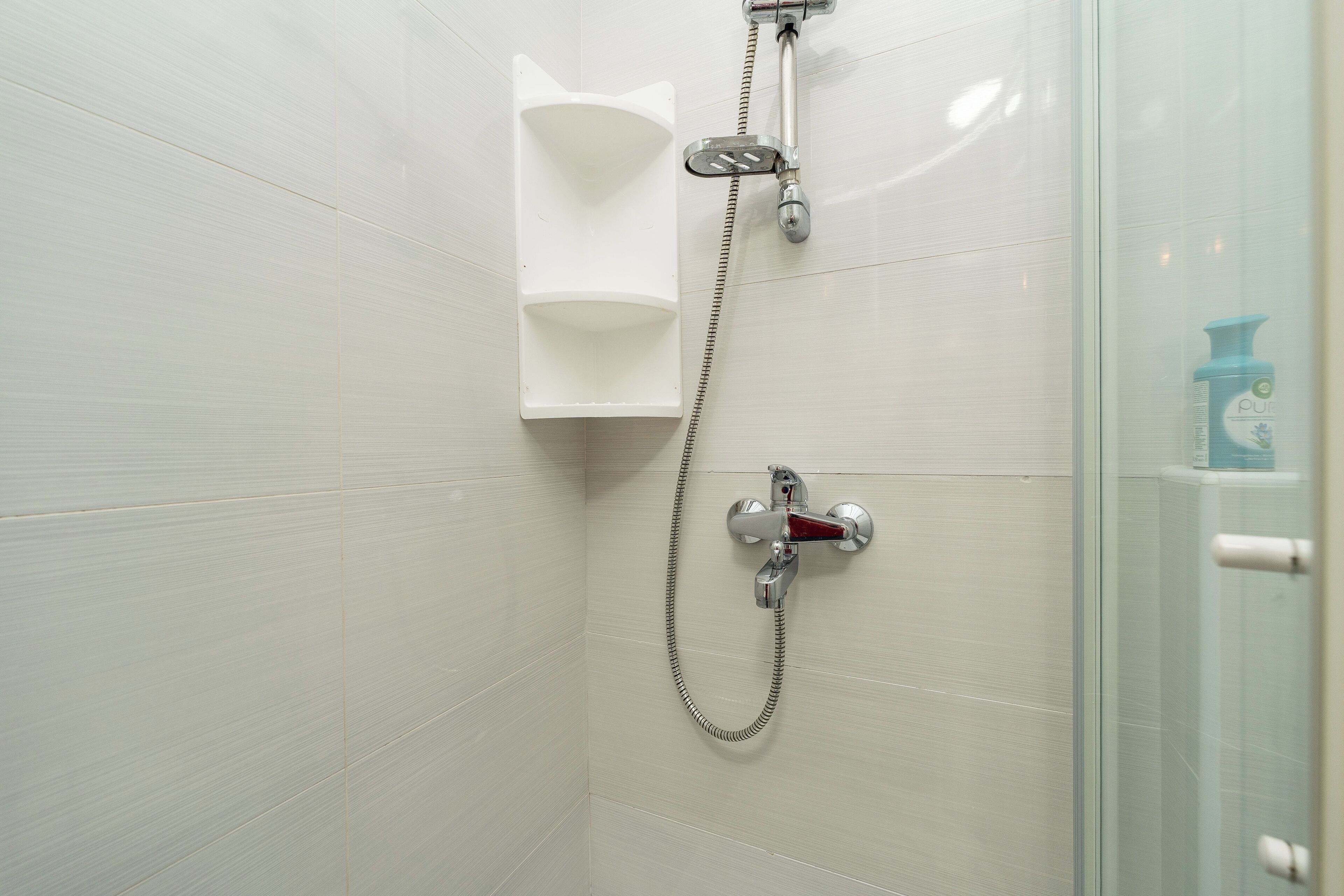 Une douche équipée d’un pommeau de douche à main, d’un robinet mural et d’un distributeur de savon.