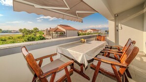 Ein Balkon mit Tisch und Stühlen, Blick auf Häuser und Grünflächen, und ein großer Sonnenschirm.