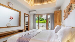 A bedroom with a large bed, a wooden headboard, a bedside table, a wall clock, and a view of the outdoors through a sliding glass door. - Peaceful Luxe Villa near Beach in Pecatu (Pecatu)